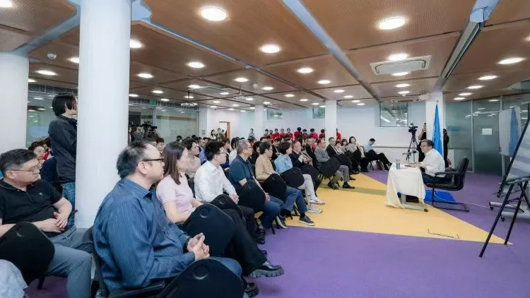 Audience seated inside UNU Macau during the Wang Defeng lecture, with a speaker at a small table and a UN flag visible on the right