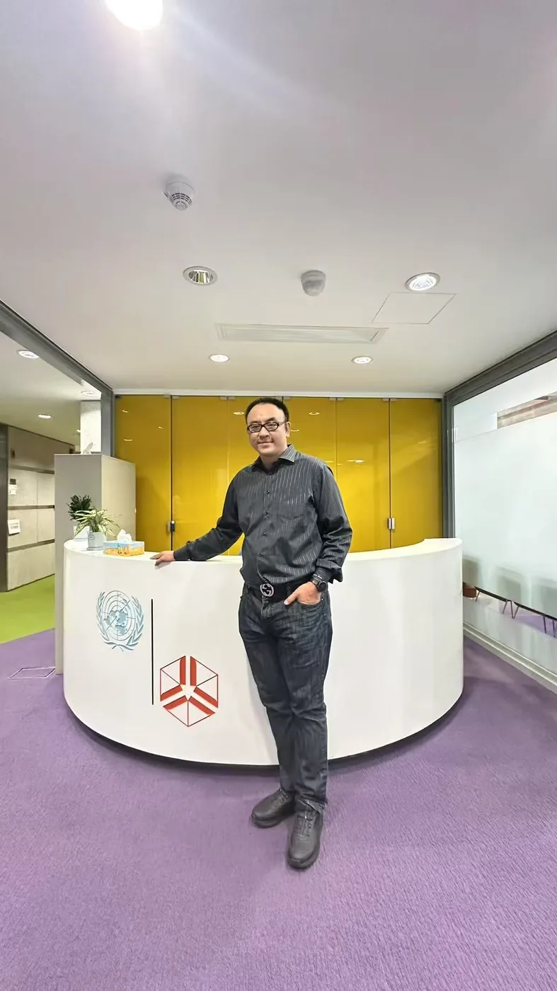Sean Own standing at the UNU Macau reception desk with the UN and UNU logos visible on the front