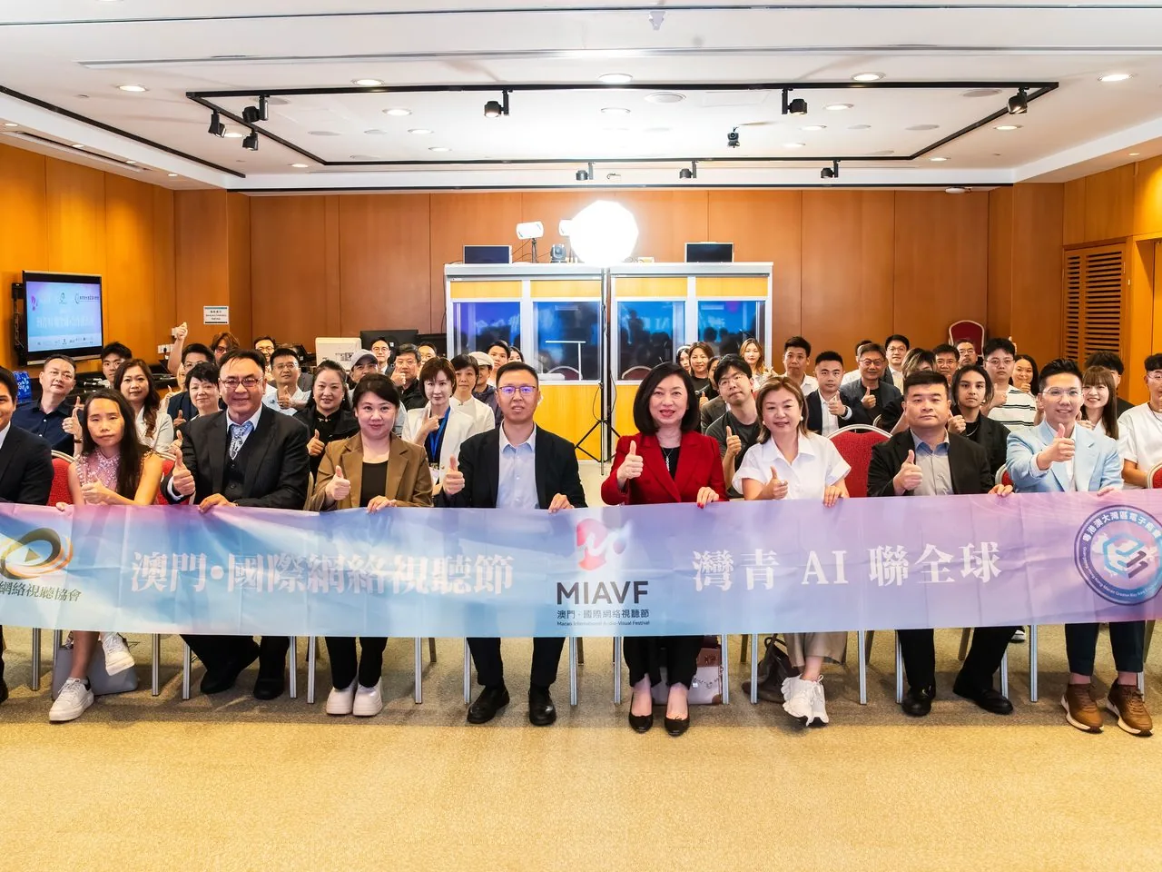 Group photo of 25+ Bay Youth AI delegates inside the Macao Science Centre auditorium giving thumbs-up behind the MIAVF banner, 2 June 2026