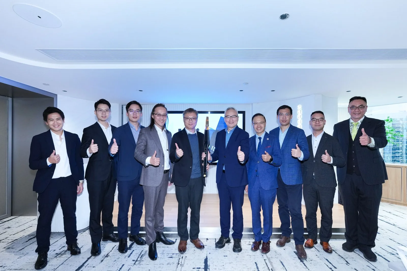 Wide-angle view of the Macau AI for All forum — speaker on stage, six delegates seated in a circle, bright bay-window in the back.